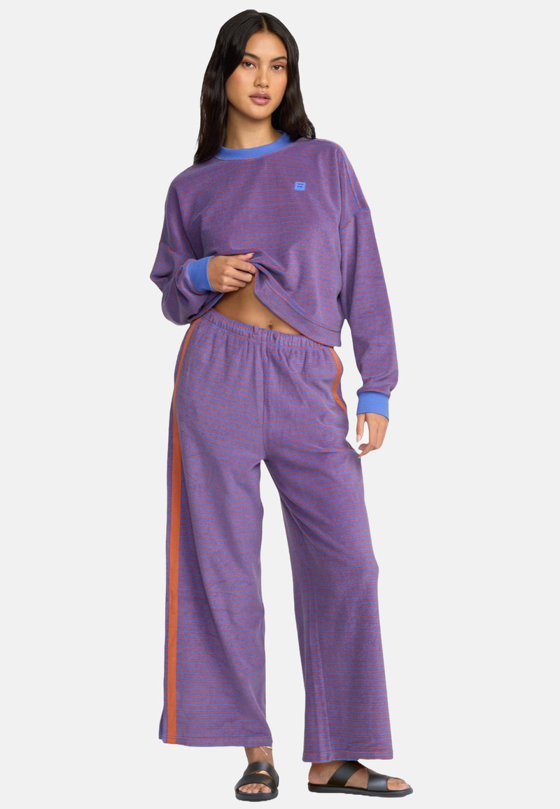 Conjunto de ropa de estar por casa a rayas moradas que incluye un top de manga larga recortado con acentos azules y pantalones de pierna ancha con paneles laterales naranjas.