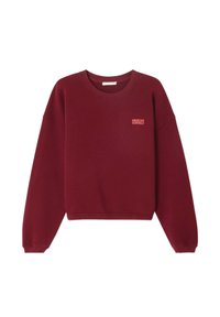 Bordo spalvos megztinis iš polaro medžiagos, su apvaliu iškirpimu, nusileidusiomis petnešomis ir mažai išsiuvinėta logo kairėje krūtinės pusėje.