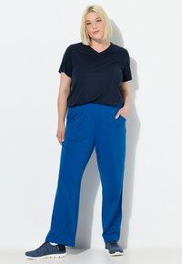 Marinblå V-ringad t-shirt i kombination med löst sittande, ljusblå byxor med sidfickor. Modellen har på sig grå sportskor.