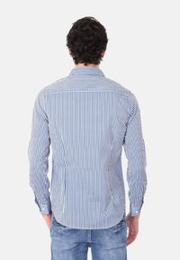 Camicia a righe blu e bianche, con maniche lunghe, colletto e orlo arrotondato. Il tessuto sembra leggero e liscio.