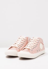 Růžové vysoké tenisky vyrobené z měkkého, lesklého materiálu. Obsahují bílé šňůrky a gumové podrážky s žebrovanou texturou. Detail na bočním zipu.