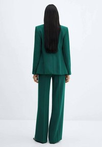 Groen op maat gemaakt pak met een gestructureerde blazer en wijde broek, gemaakt van een zachte stof, met een strak design en subtiele textuur.