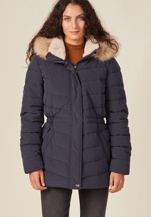 Piumino blu navy con cappuccio foderato in pelliccia sintetica, trapuntato orizzontalmente, vita affusolata e due tasche frontali. Texture morbida e materiale resistente.