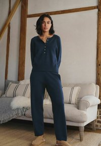Navy blue knit lounge set features a long-sleeve top with a Henley neckline and button detail, paired with relaxed-fit trousers.