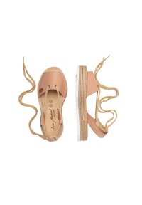 Zapatos espadrilles de cuero color beige claro con cintas trenzadas en el tobillo, suela de goma blanca y detalles de yute en la base. Parte superior de cuero texturizado.