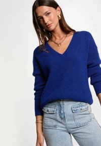 Maglione blu a maglia con scollatura a V e texture a costine. Abbinato a jeans a vita alta in denim chiaro con tasche frontali.