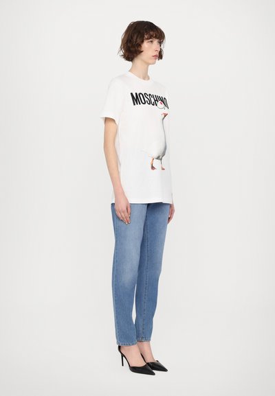 Balta medvilninė marškinėliai su žąsies grafika ir "MOSCHINO" tekstu. Derinama su šviesiai mėlynomis džinsomis ir juodais smailiais kulnais.