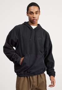 Črna kapuca z flis telesom in gladkim spodnjim žepom. Ima elastične manšete in vrvico. Nike logotip v toniranem šivu.