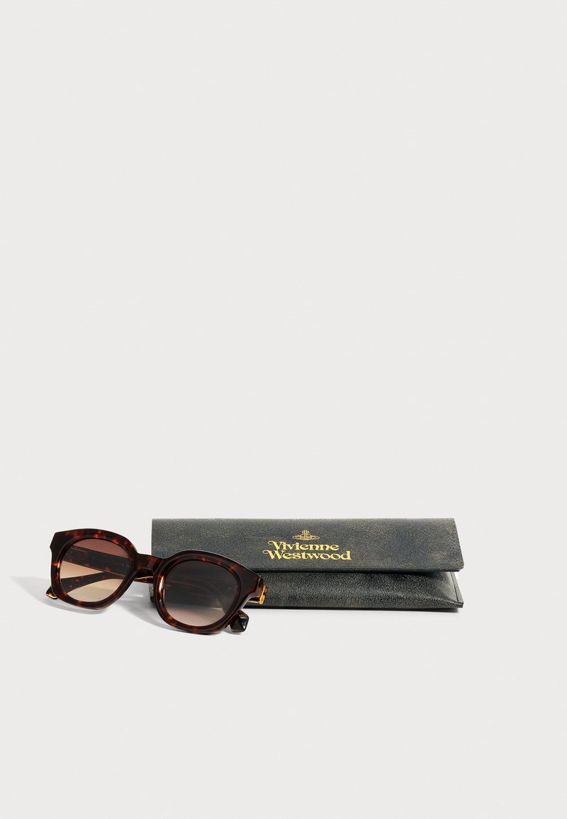 Quadratische Sonnenbrille mit Schildpatt-Fassung und braunen Verlaufs-Gläsern neben einem schwarzen Lederetui mit Vivienne Westwood-Logo auf einer weißen Oberfläche.
