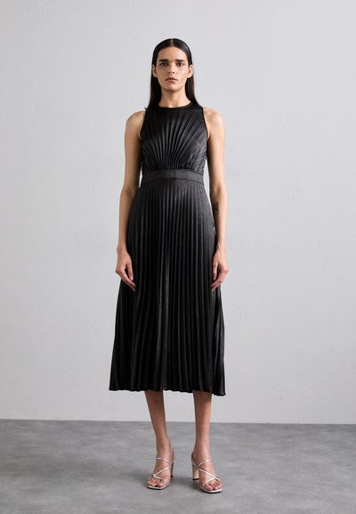Rochie midi neagră plisată, cu un corset ajustat, decolteu rotund și talie lată. Asortată cu sandale argintii cu bretele.