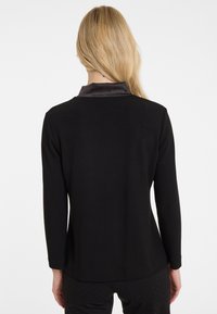 Schwarzes langärmliges Oberteil mit einem strukturierten Satin-Kragen, das ein glattes, tailliertes Design und einen leicht abgerundeten Saum hinten aufweist.