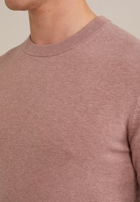 Suéter de punto rosa claro con cuello redondo y puños de canalé. La tela tiene una textura suave y un acabado liso. Vista en primer plano del hombro.