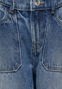 Blaue Denim-Jeans mit hoher Taille, Vordertaschen und sichtbaren Nähten. Das Material ist weich mit einem verwaschenen Finish und einer strukturierten Optik.