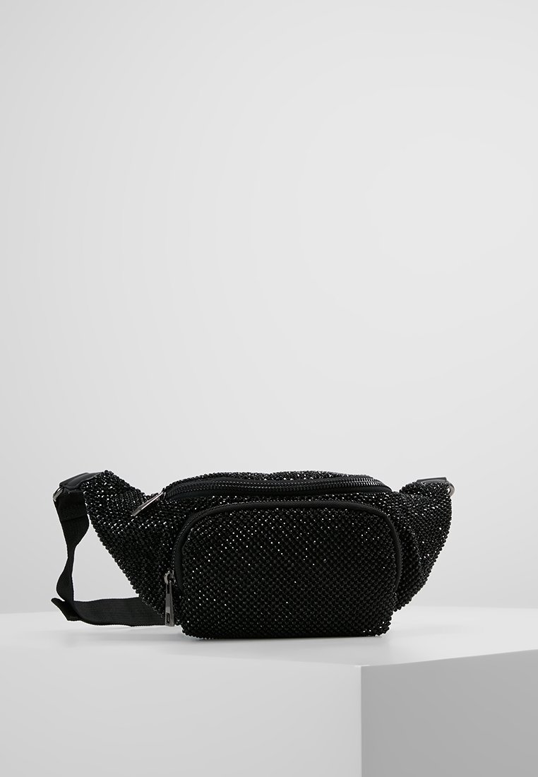 Sac banane en tissu noir couvert de petites perles noires, avec une poche zippée à l'avant et une sangle noire réglable, présenté sur une surface blanche.