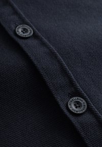 Maglione di lana blu scuro con tessuto testurizzato, chiusure a bottone con finitura in plastica nera e scollo liscio e pulito.