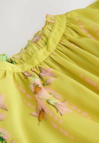 Tissu léger jaune avec imprimé floral rose et détail de col à volants.