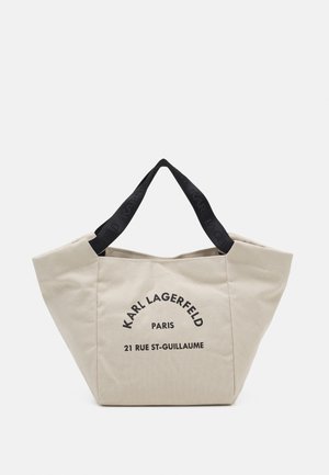 Beige lærredstaske med sorte dobbelthåndtag. Har trykt tekst: "KARL LAGERFELD PARIS 21 RUE ST-GUILLAUME" på fronten.