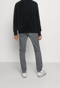 Zwarte gebreide trui met textuur, grijze broek en witte sneakers met minimale accenten. Focus op pasvorm en strakke lijnen, gezien van achteren.