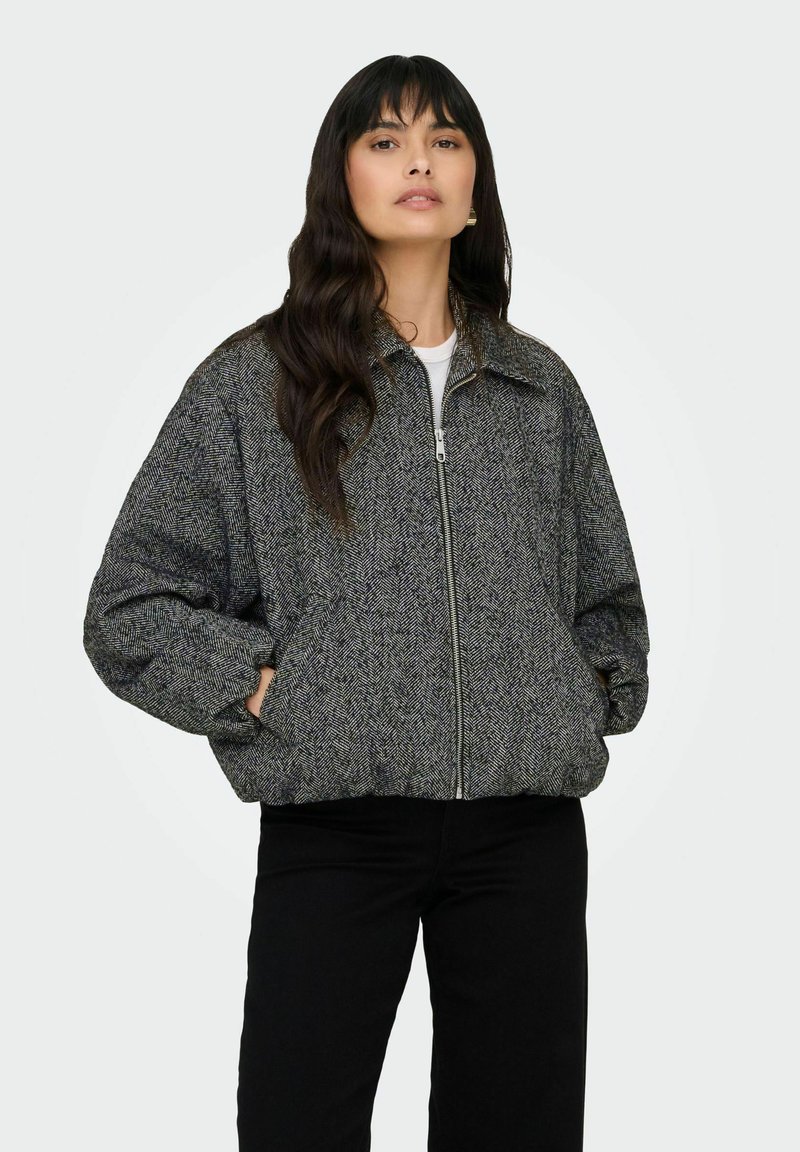 Veste grise à motif chevron avec fermeture éclair, coupe décontractée et poches latérales. Dispose d'un col à revers et d'un tissu doux et texturé.