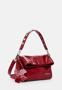 Rote Leder-Schultertasche mit umklappbarem Deckel, verziertem Riemen und einem floralen Charm. Verfügt über eine glänzende Oberfläche und silberne Hardware-Akzente.
