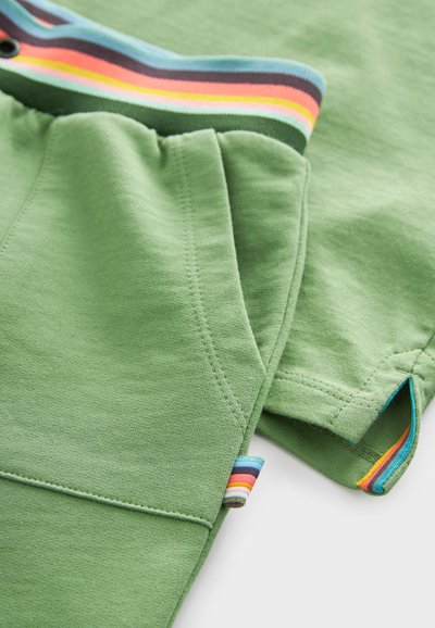 Zaļi kokvilnas šorti ar svītrainu jostu, kurā ir zilas, melnas, oranžas un sarkanas akcenti. Gluda tekstūra un brīvas formas dizains.