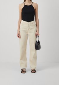 Top halter nero a coste con bordi scallop, abbinato a jeans a palazzo beige chiaro a vita alta. Borsa nera e sandali con cinturini.