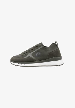 Sneaker de sport en gris foncé avec des matériaux en maille et en daim, bout arrondi, lacets et semelles blanches. Présente un logo sur le côté.