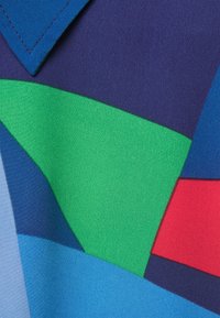 Kolorowa, wzorzysta tkanina z niebieskimi, zielonymi, granatowymi i czerwonymi kształtami. Gładka tekstura z wyraźnymi blokami kolorów i precyzyjnymi szwami.