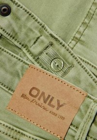Zeleni traper tkanina s vidljivim šavovima, dugmetom i smešnim etiketom na smešnom čitanju "ONLY Blue Denim anno 1995." Etiketa ima prošivene ivice.