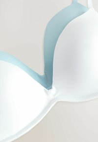 Hvid og lyseblå BH med glat stof, formede skåle og justerbare stropper. Har et sømløst design og blød tekstur.