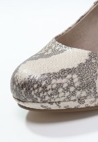 Gros plan sur une ballerine à motif peau de serpent argentée et grise, avec un bout arrondi et une doublure intérieure beige.
