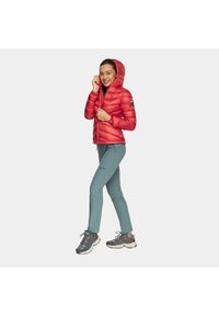 Czerwona kurtka puchowa z kapturem i elastycznym dołem, w połączeniu z jasnobłękitnymi, dopasowanymi spodniami i szarymi butami hikingowymi z ciemnymi akcentami.