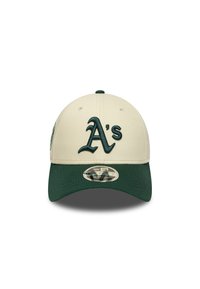 Casquette de baseball beige avec une visière vert foncé. Présente un logo "A's" brodé à l'avant et un logo circulaire sur le côté. Tissu texturé.