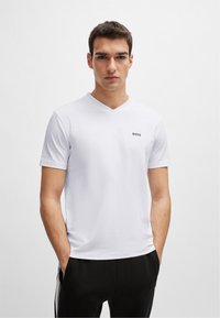 T-shirt bianco a maniche corte con scollatura a V in tessuto morbido, con un piccolo logo nero "BOSS" sul petto. Abbinato a pantaloni neri.
