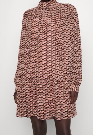 Vestido de manga larga y cuello alto con patrón geométrico rosa y negro, de corte holgado y dobladillo con volantes, usado por una persona de piel oscura.