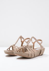 Sandales beiges à talon compensé, avec un design à plusieurs sangles et des accents en chaîne métallique. Fabriquées en doux suède.