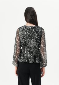 Schwarze florale Peplum-Bluse mit durchsichtigen langen Ärmeln, gerafftem Taillenbund und zartem weißen Blumenmuster. Weicher, leichter Stoff.