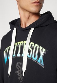 Sort hættetrøje med et stort "WHITE SOX" grafik i gradientfarver fra gul til blå. Har hvide snore og en blød tekstur.