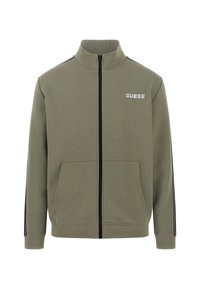 Olivovo zelená zipsová bunda z jemného materiálu, s dvoma prednými vreckami, čiernymi bočnými pruhmi a bielym logom "GUESS" na hrudi.