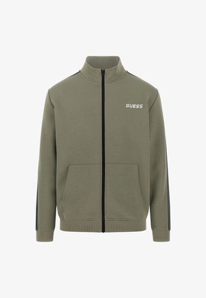 Olivgrüne Zip-Jacke aus weichem Material mit zwei Vordertaschen, schwarzen Seitennähten und einem weißen "GUESS"-Logo auf der Brust.