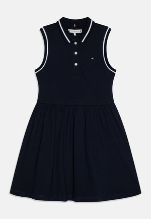 Granatowa sukienka typu polo bez rękawów z kołnierzykiem, trójrzędowym zapięciem na guziki i białymi akcentami wzdłuż kołnierza oraz otworów na rękawy.