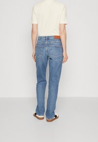 Jeans de mezclilla azul claro con un corte relajado, dos bolsillos traseros y una etiqueta de cuero marrón en la cintura. Estilo casual, de largo hasta el tobillo.