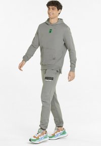 Grå hættetrøje med et grønt grafisk motiv, frontlomme. Grå sweatpants med "PUMA MINECRAFT" logo. Farverige sneakers, blanding af grøn og brun.