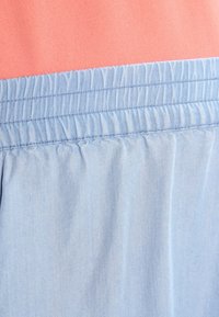 Blåt elastisk bånd på lyseblåt stof mod en laksefarvet baggrund, der viser rynkede og syede detaljer.