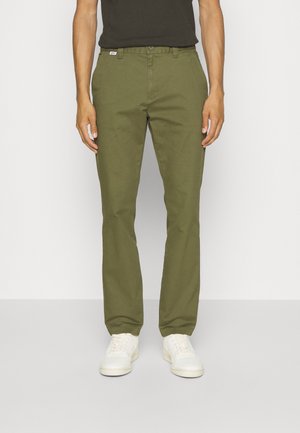 Chinos in cotone verde oliva con vestibilità dritta, dotati di chiusura con bottone, passanti per cintura e tasche laterali. Abbinati a sneakers bianche.