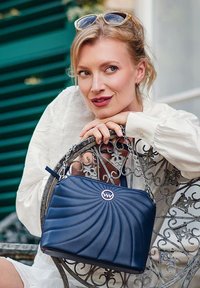 Tmavě modrá kabelka s prošívaným vířivým vzorem, kožený materiál, řetízkový popruh a kulatý detail loga na přední straně.