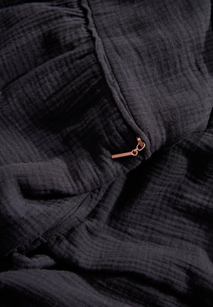 Zwart tekstiel met een gekreukeld uiterlijk, met een klein bronzen ritsdetail. Zacht, lichtgewicht materiaal met subtiele patronen.