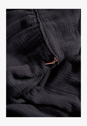 Tissu noir texturé avec une apparence froissée, présentant un petit détail de zip en bronze. Matière douce et légère avec des motifs subtils.