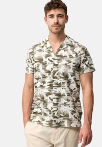 Chemise à manches courtes en tissu léger, présentant un motif abstrait vert et blanc, un design sans col et des détails de bouton à l'avant.