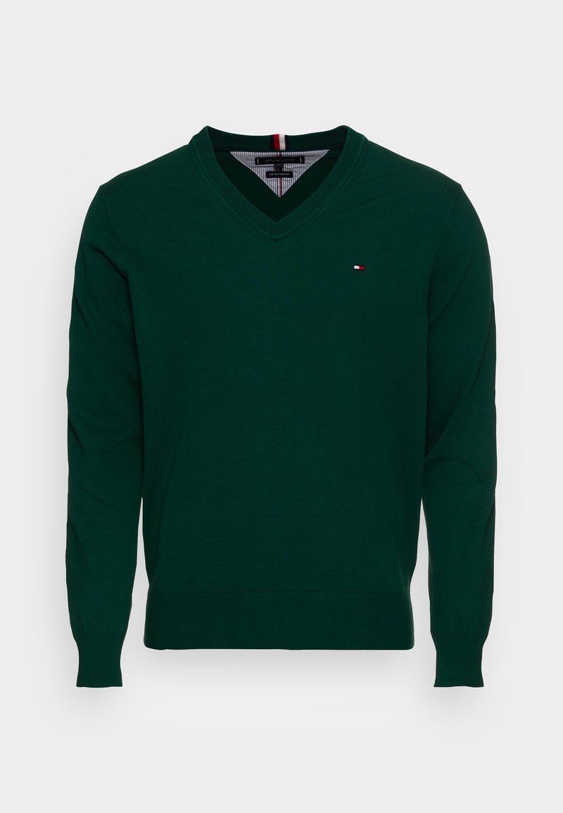 Pull vert foncé à col en V avec manches longues et un petit logo rouge, blanc et bleu sur le côté gauche de la poitrine.